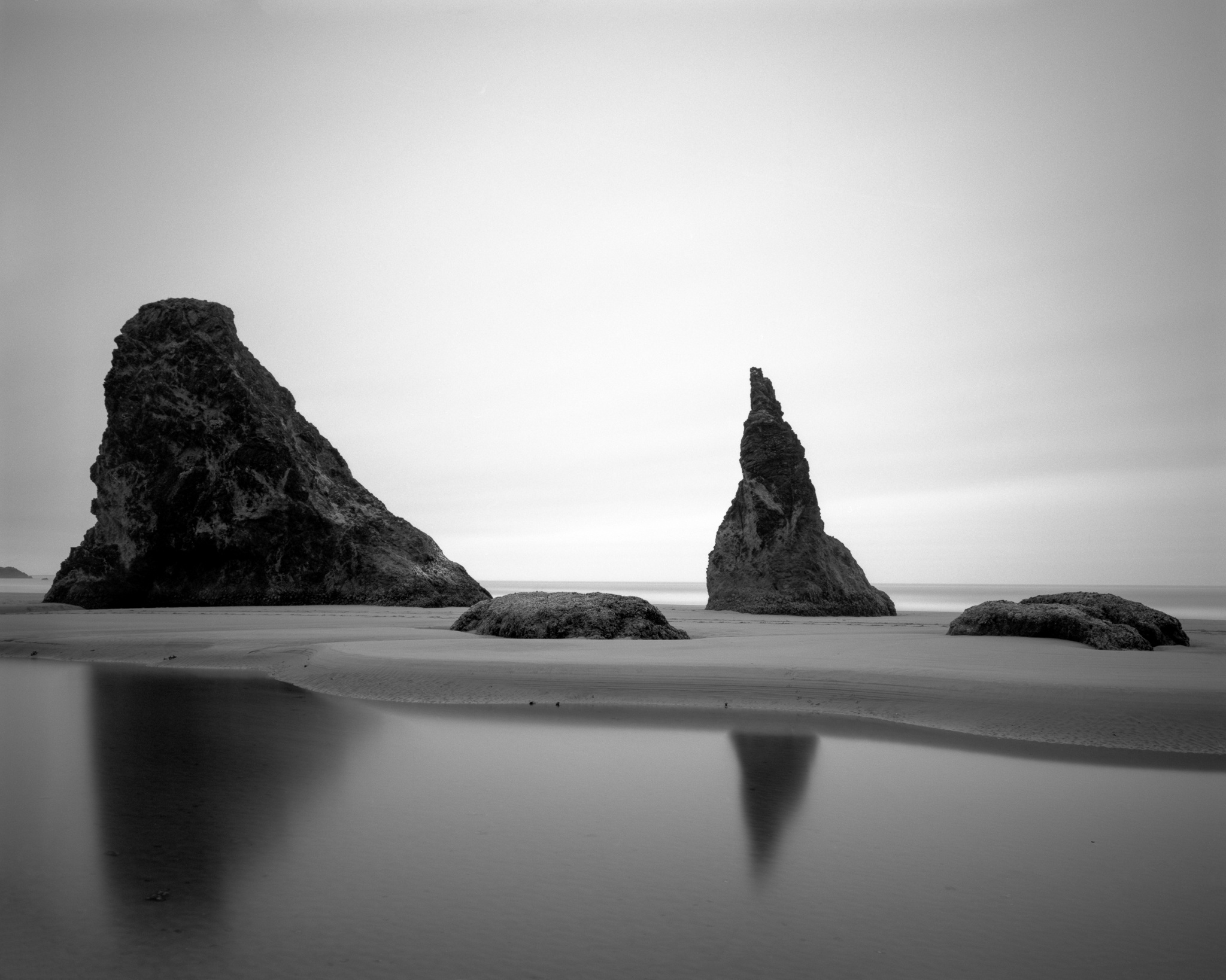 Two sea stacks rise from a glassy foreground at Bandon Beach in this long exposure black and white study of the Oregon coast, California. Photograph by Marty Quinn