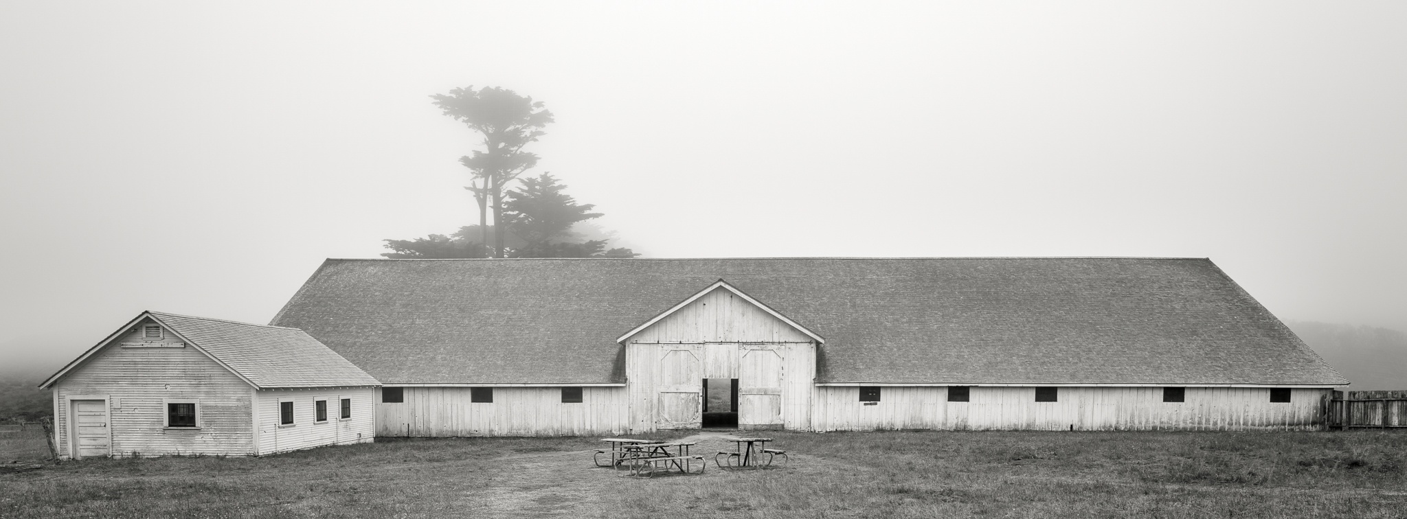 A large hay barn emerges from morning fog in the rural American countryside, California. Photograph by Marty Quinn